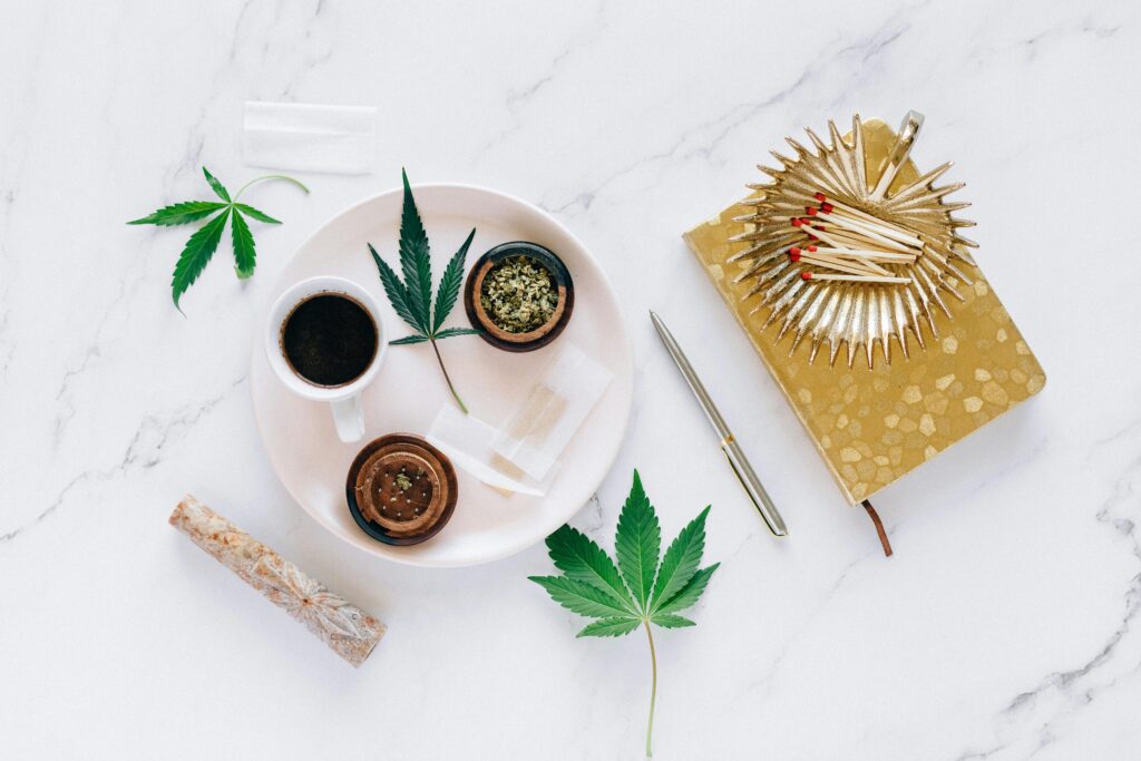 Top view of cannabis leaves, coffee, grinder, and matches on a marble surface, creating a relaxed setting.